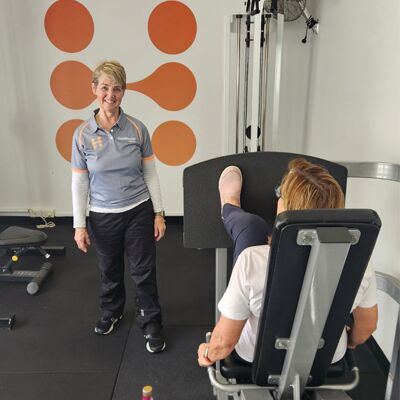 Healthspan Collective โ Female personal trainer guiding a client on the leg press machine.